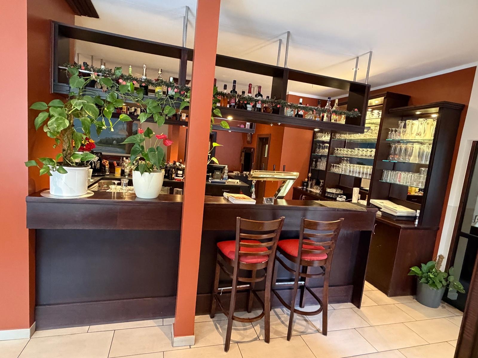 Gemütliche Bar im Restaurant Santa Lucia mit dunklem Holztresen, Barhockern und gut sortiertem Getränkeregal