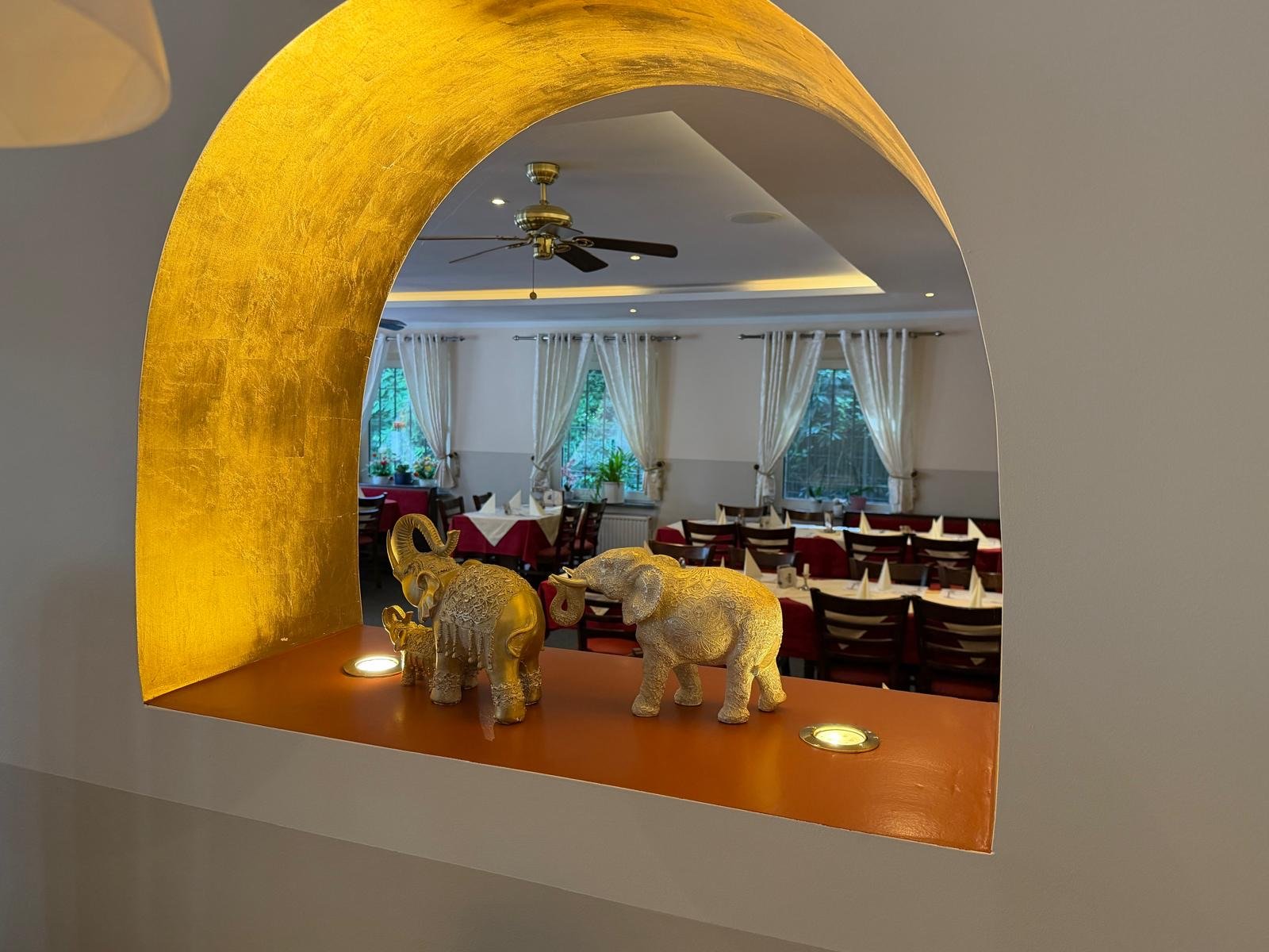 Goldene Elefanten-Dekoration in einer beleuchteten Wandnische mit Blattgold-Bogen